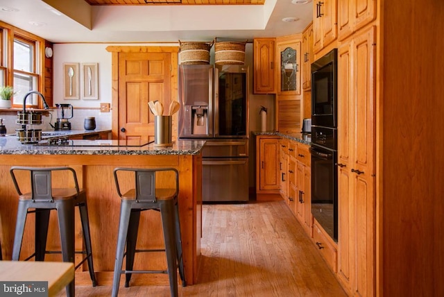 kitchen with black appliances, a breakfast bar, a tray ceiling, and a sink