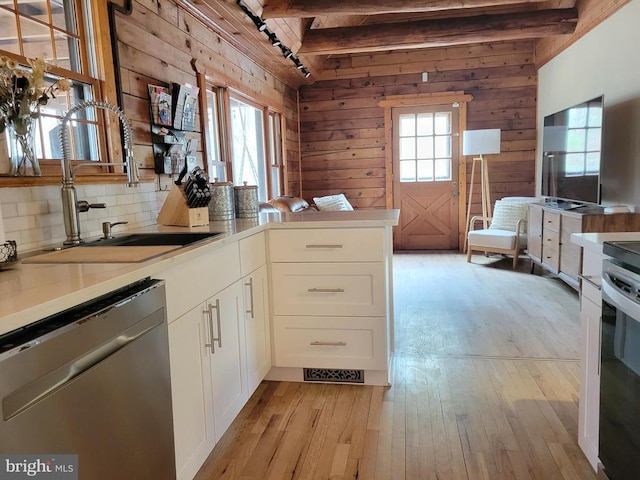 kitchen featuring beam ceiling, light wood-style flooring, white cabinets, a sink, and dishwasher