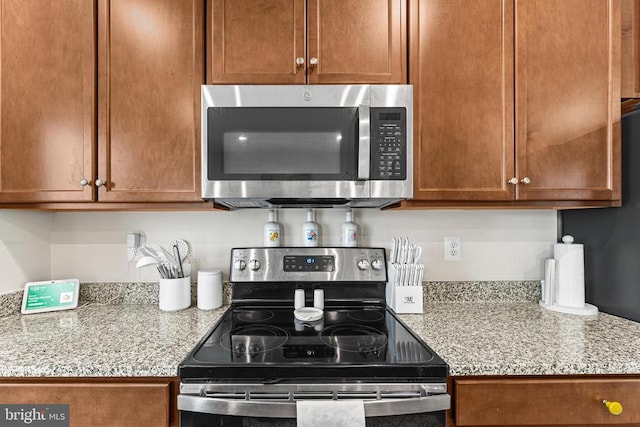 kitchen with light stone countertops, appliances with stainless steel finishes, and brown cabinetry