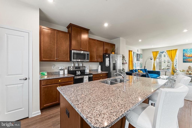 kitchen featuring wood finished floors, a sink, a kitchen breakfast bar, appliances with stainless steel finishes, and a center island with sink