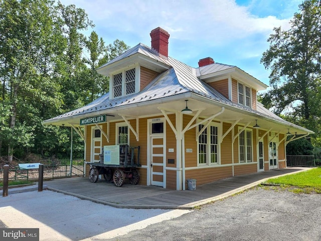 exterior space with fence, covered porch, a chimney, a standing seam roof, and metal roof