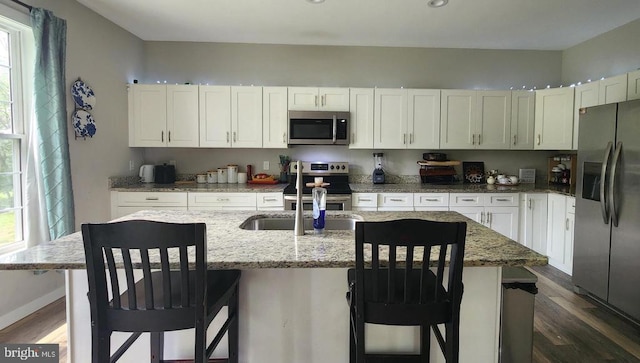 kitchen with appliances with stainless steel finishes, white cabinets, dark wood-style flooring, and light stone counters