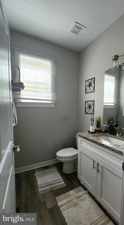 bathroom featuring vanity, toilet, a healthy amount of sunlight, wood finished floors, and visible vents