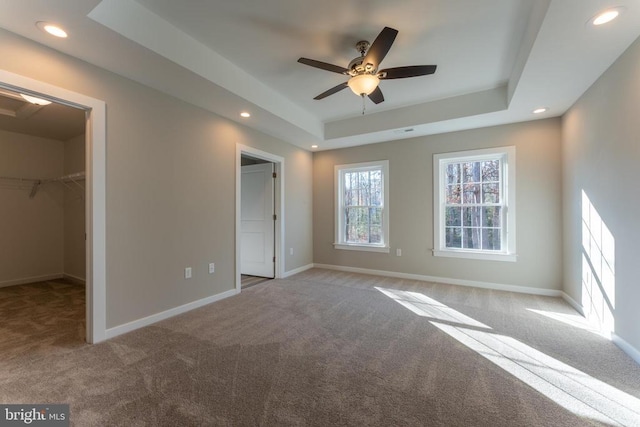 unfurnished bedroom with baseboards, a walk in closet, recessed lighting, a raised ceiling, and carpet flooring