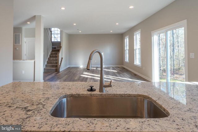 interior details with wood finished floors, a sink, light stone counters, baseboards, and recessed lighting