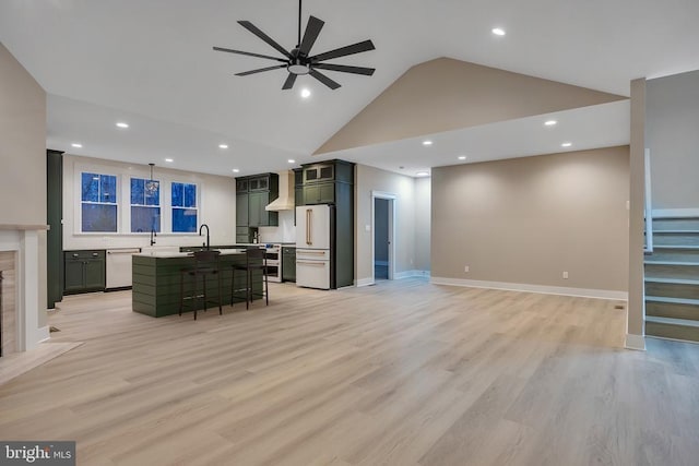 living room featuring sink, a premium fireplace, ceiling fan, high vaulted ceiling, and light wood-type flooring