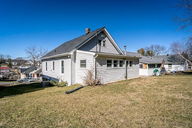 rear view of property with central air condition unit, a chimney, and a yard