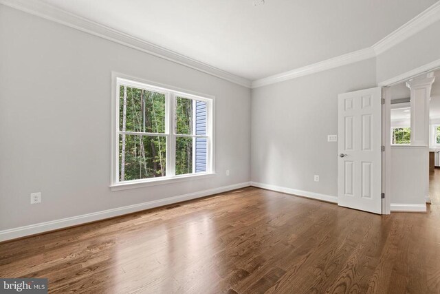 empty room featuring crown molding, dark wood-type flooring, and ornate columns