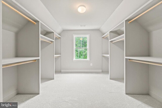 walk in closet with light colored carpet and lofted ceiling