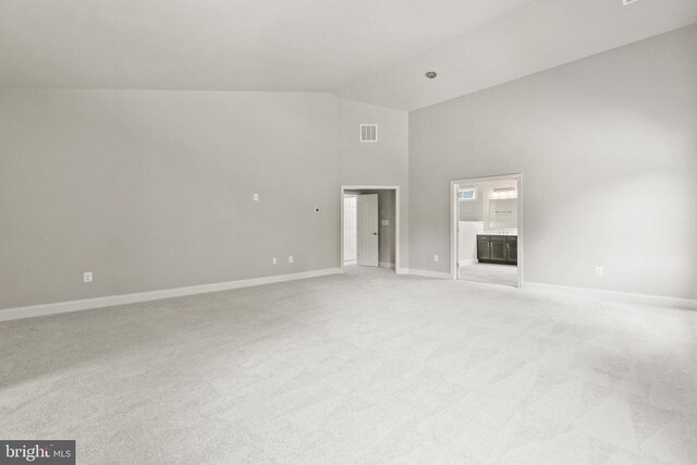 unfurnished living room with high vaulted ceiling and light colored carpet