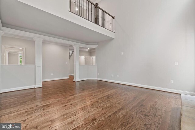 unfurnished living room featuring a towering ceiling, hardwood / wood-style floors, and decorative columns