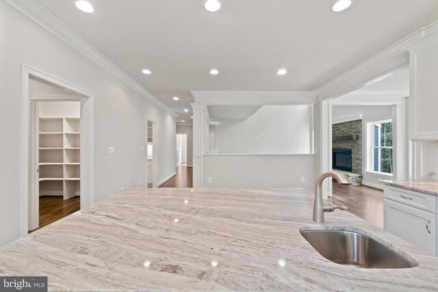 kitchen featuring dark hardwood / wood-style floors, a fireplace, white cabinetry, sink, and light stone counters