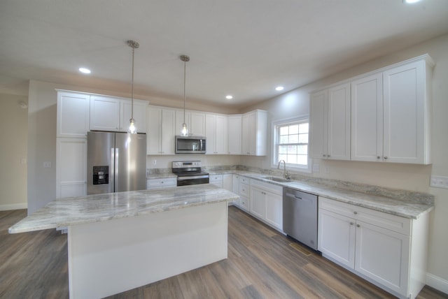 kitchen featuring white cabinets, a kitchen island, appliances with stainless steel finishes, decorative light fixtures, and a sink