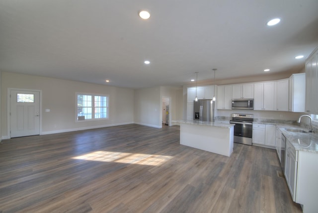 kitchen with stainless steel appliances, a sink, white cabinetry, open floor plan, and a center island