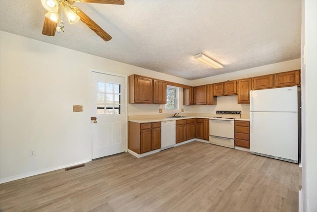 kitchen featuring sink, white appliances, a textured ceiling, and light wood-type flooring