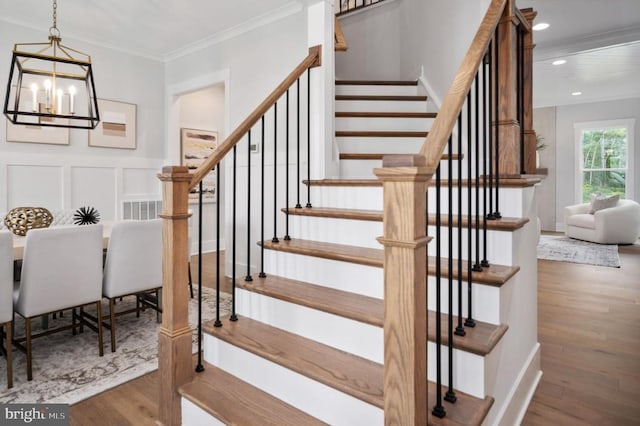 stairs featuring ornamental molding, a chandelier, a decorative wall, and wood finished floors