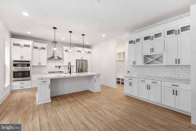 kitchen featuring white cabinetry, light countertops, appliances with stainless steel finishes, an island with sink, and glass insert cabinets