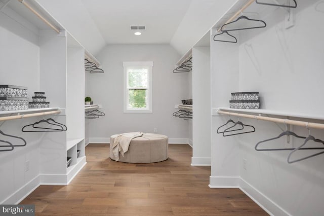 spacious closet with lofted ceiling, visible vents, and wood finished floors