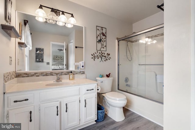 full bathroom with hardwood / wood-style flooring, backsplash, bath / shower combo with glass door, vanity, and toilet