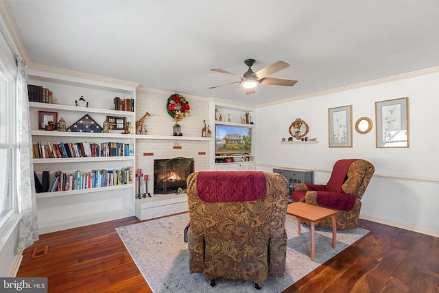 living area with dark hardwood / wood-style flooring, ornamental molding, ceiling fan, a brick fireplace, and built in shelves