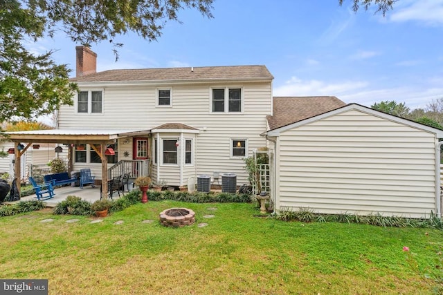 rear view of house with cooling unit, a yard, a patio area, and an outdoor fire pit