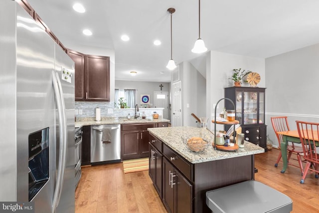 kitchen featuring hanging light fixtures, light wood-style flooring, appliances with stainless steel finishes, a kitchen island, and a sink