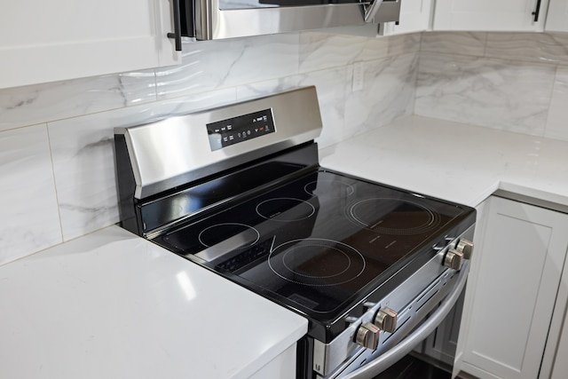 kitchen featuring stainless steel range with electric stovetop, light stone countertops, decorative backsplash, and white cabinets