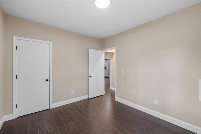 unfurnished bedroom featuring dark wood-type flooring and stainless steel refrigerator with ice dispenser