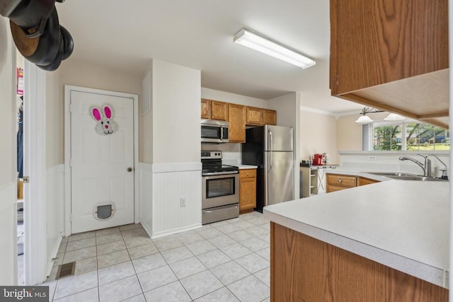 kitchen featuring brown cabinets, light countertops, a sink, wainscoting, and appliances with stainless steel finishes