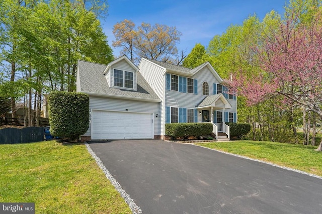 colonial-style house with an attached garage, roof with shingles, a front yard, and aphalt driveway