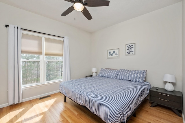 bedroom with ceiling fan, visible vents, baseboards, and wood finished floors