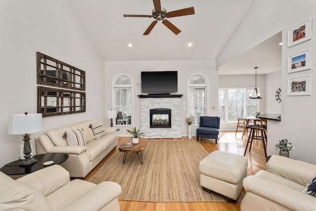 living area with recessed lighting, a stone fireplace, ceiling fan with notable chandelier, and wood finished floors