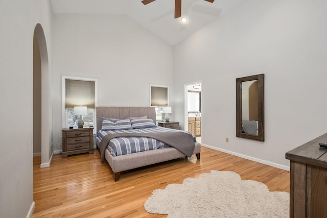 bedroom with arched walkways, high vaulted ceiling, light wood-type flooring, and baseboards