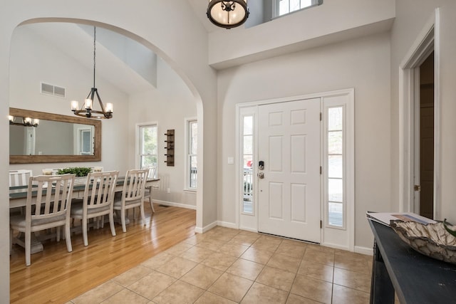 entrance foyer featuring light tile patterned floors, baseboards, visible vents, high vaulted ceiling, and a chandelier