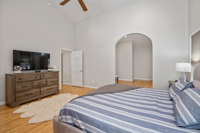 bedroom with baseboards, arched walkways, high vaulted ceiling, and light wood finished floors