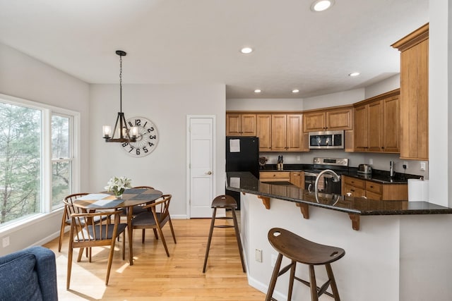 kitchen with light wood finished floors, a kitchen breakfast bar, brown cabinetry, stainless steel appliances, and a sink