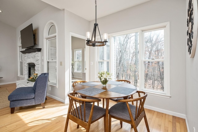 dining room featuring a stone fireplace, a notable chandelier, baseboards, and light wood finished floors