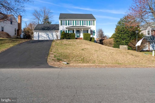 colonial house with aphalt driveway, a garage, and a front lawn