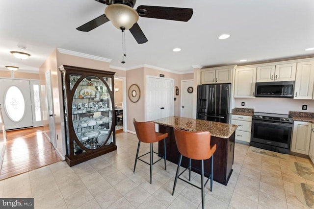 kitchen featuring stainless steel microwave, cream cabinetry, electric range oven, and black fridge