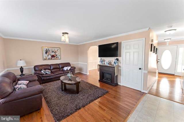 living area featuring light wood-type flooring, arched walkways, a fireplace, and crown molding