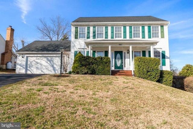 colonial house with covered porch, an attached garage, driveway, and a front lawn