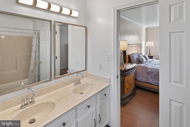 ensuite bathroom featuring double vanity, wood finished floors, crown molding, and a sink