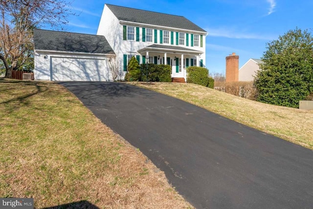 colonial home with a porch, driveway, a front yard, and a garage