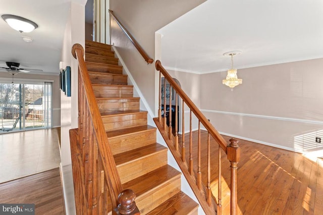 stairs featuring baseboards, ceiling fan with notable chandelier, wood finished floors, and ornamental molding