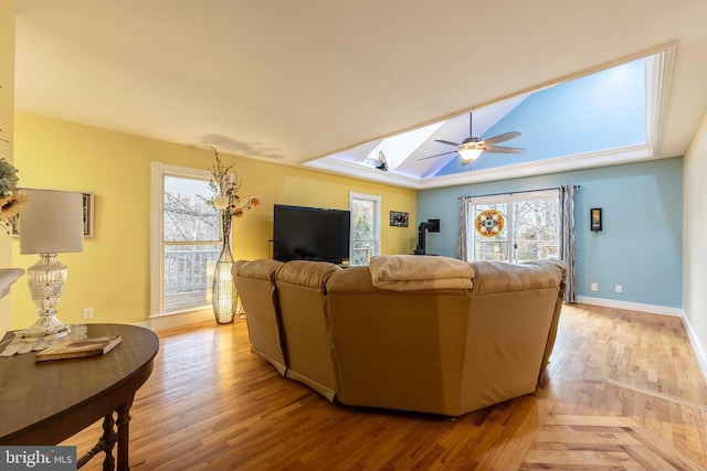 living room featuring baseboards, a ceiling fan, light wood finished floors, and a skylight