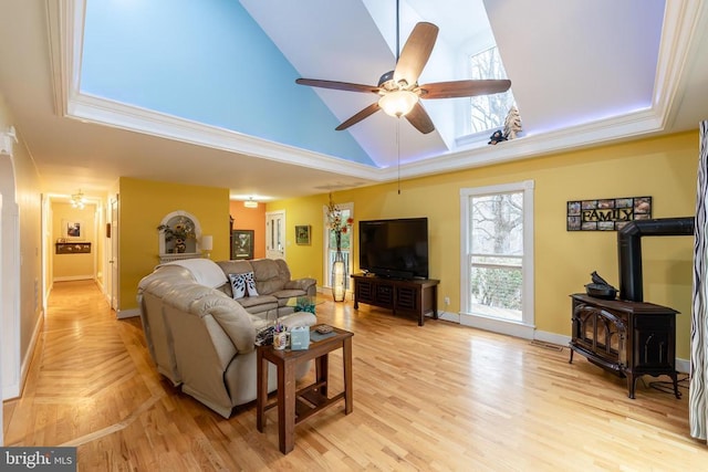living area with light wood-style flooring, baseboards, ceiling fan, high vaulted ceiling, and a wood stove