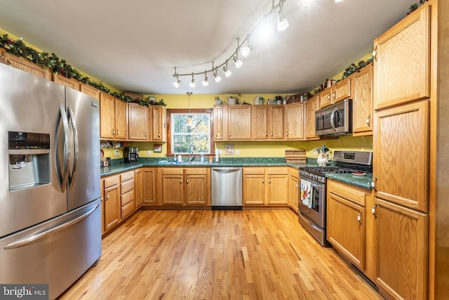 kitchen featuring dark countertops, appliances with stainless steel finishes, a sink, and light wood-type flooring
