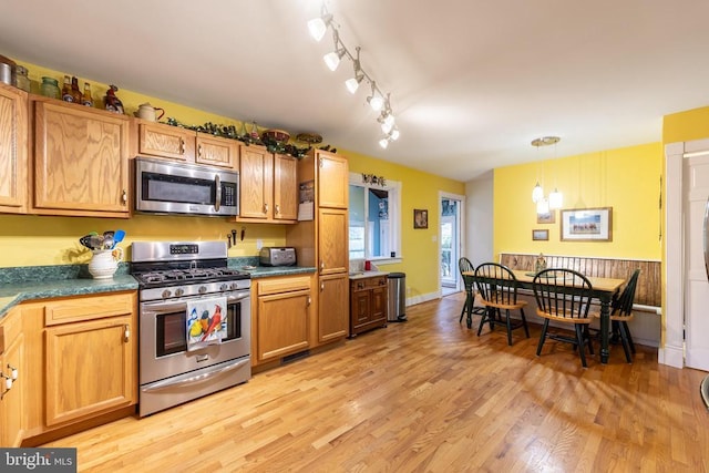 kitchen with dark countertops, light wood-style floors, pendant lighting, rail lighting, and appliances with stainless steel finishes