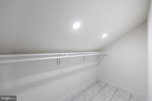 walk in closet with marble finish floor and lofted ceiling