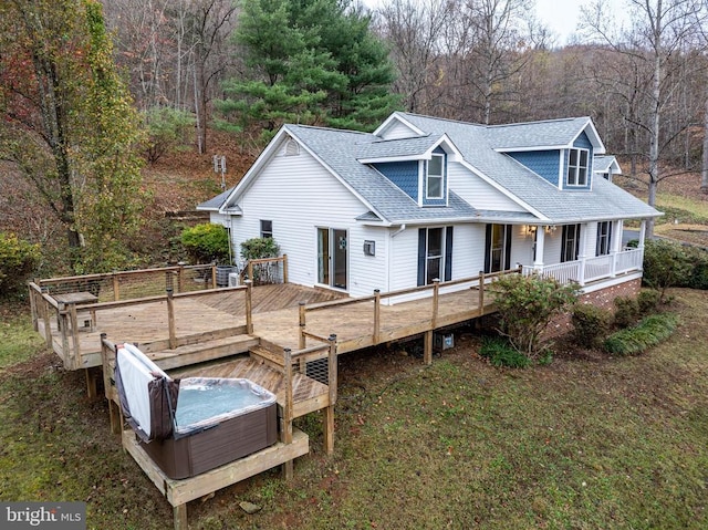 rear view of property featuring central AC, a forest view, covered porch, a hot tub, and roof with shingles